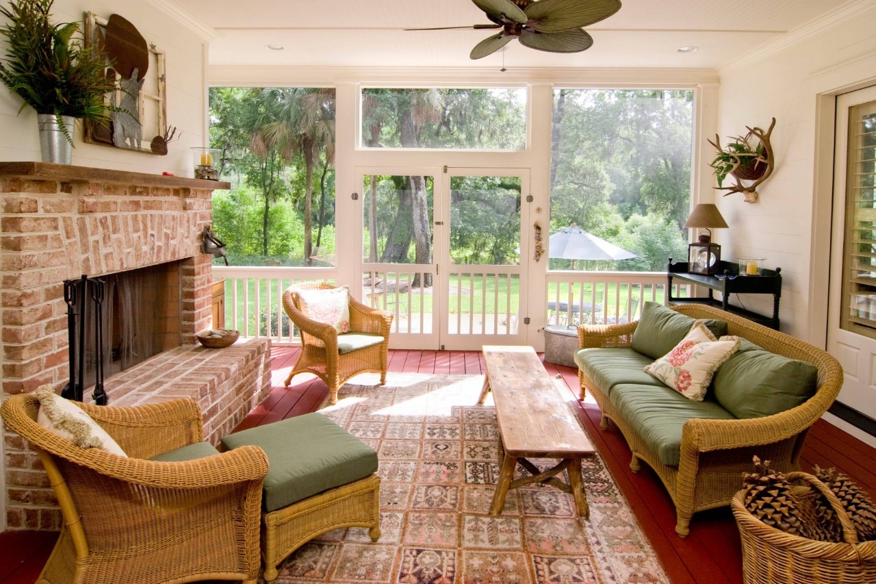 A traditional sunroom with wicker furniture, a brick fireplace, and large windows and French doors at Delux Drapery & Shade Co. near Ann Arbor, MI